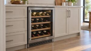 A built-in wine cooler installed under a kitchen counter with its glass door closed, bottles visible inside