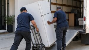 Two movers tilting a refrigerator onto a hand truck beside a moving truck
