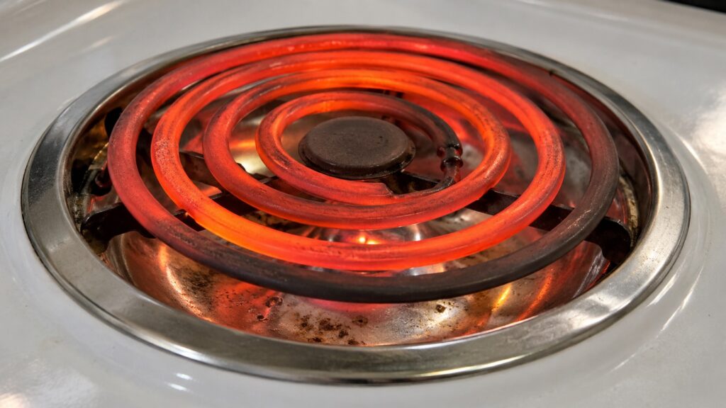A close view of one glowing red coil element on an electric range cooktop with a shallow drip bowl beneath it