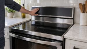 A freestanding electric range with its dark touch control panel switched off and a hand resting near the keypad